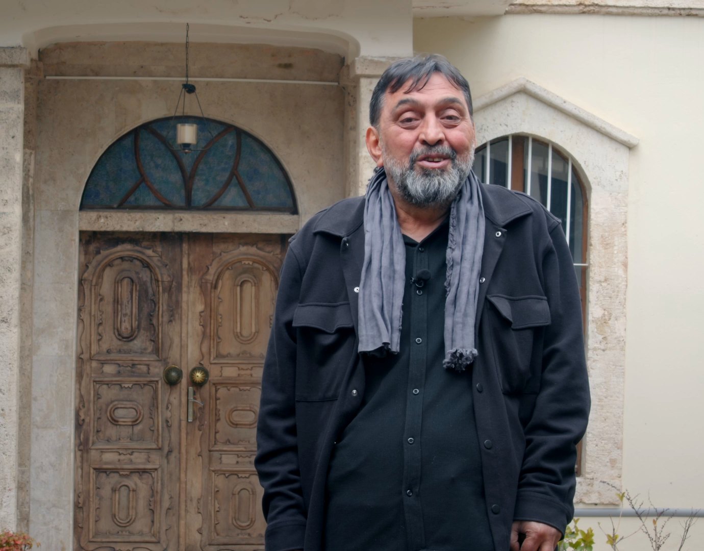 Ahmet Yenilmez, fesli ve gri takımlı; başını hafifçe çevirmiş, bakışı kameranın ötesinde